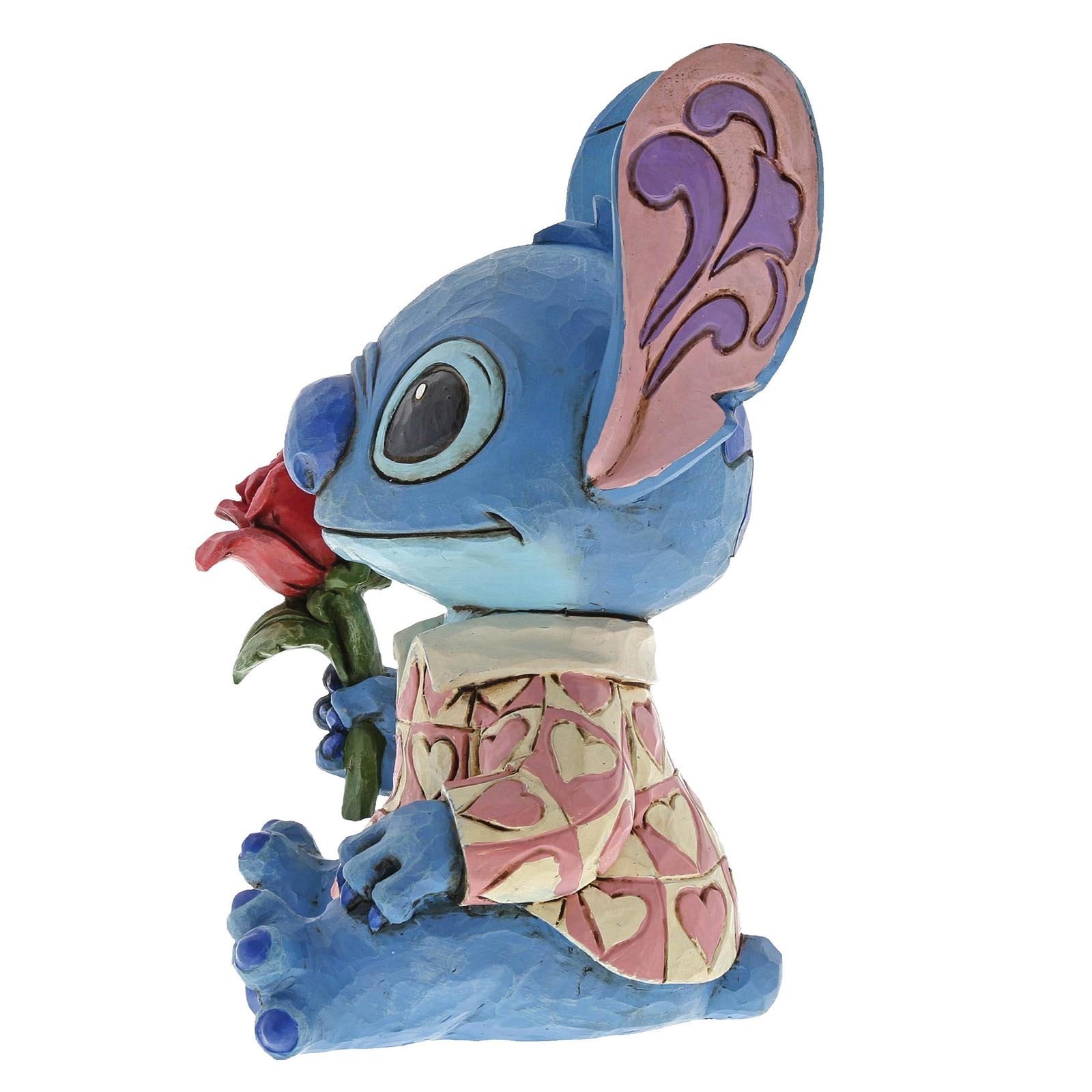 Detail van Stitch als 'Clueless Casanova', met een bloemetje in de hand en een verlegen uitdrukking, ontworpen door Jim Shore in traditionele houtsnijstijl.