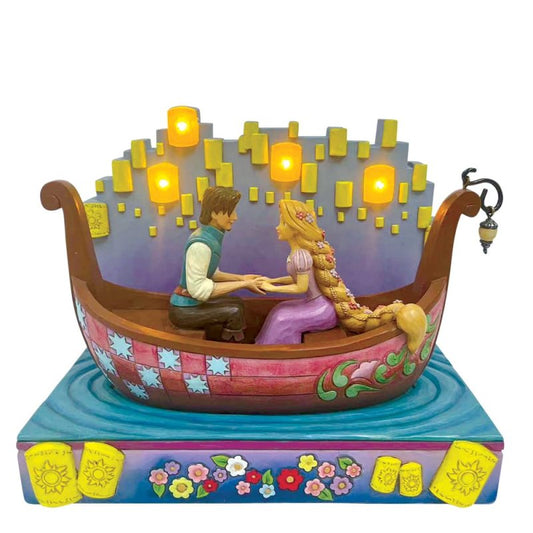 Jim Shore-beeldje van Rapunzel en Flynn Rider in een romantische boottocht tussen LED-lantaarns, met bloemen in Rapunzels haar en gedetailleerde rosemaling-patronen op de boot.
